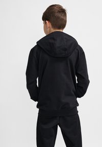 Schwarzer Hoodie mit einer Kängurutasche vorne und verstellbarem Kapuzen. Aus weichem, kuscheligem Stoff mit lockerer Passform, von hinten betrachtet.