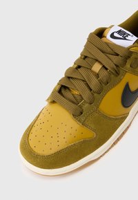 Nike tenisice s gornjim dijelom od žute kože i maslinasto zelene nubuk kože, s crnim naglasima, perforacijama i ravnim vezicama. Vidljiva gumena potplata.