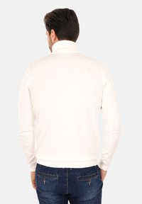 Maglione bianco a maglia con colletto alto, forma aderente e polsini a coste, abbinato a jeans in denim blu scuro. Texture liscia e dettagli minimi.