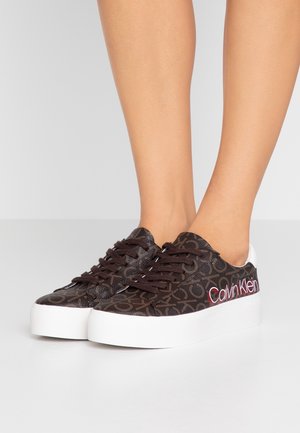 Ruskeat kuvioidut lenkkarit valkoisella kumipohjalla, joissa on ruskeat nauhat ja punainen "Calvin Klein" -logo sivussa. Teksturoitu päällismateriaali.