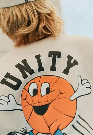 Sudadera beige clara con un gráfico central de una pelota de baloncesto naranja sonriente con brazos, acompañada por la palabra "UNITY" encima.