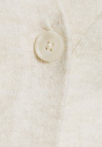Kremowy, dziany kardigan z okrągłym, plastikowym guzikiem z czterema dziurkami i miękką fakturą.