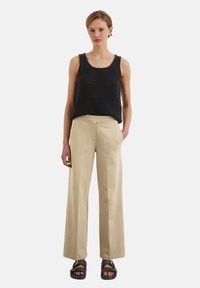 Top in maglia nera, pantaloni beige a gamba larga e sandali neri. L'outfit presenta un design semplice e casual con una vestibilità rilassata e accenti minimi.