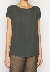 Blusa a maniche corte di colore verde scuro realizzata in tessuto morbido. Presenta un collo rotondo, una vestibilità comoda e un orlo leggermente curvo. Design semplice e pulito.