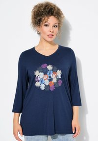 T-shirt a maniche lunghe blu navy con scollo a V, caratterizzato da una grafica floreale e dal testo "CASUAL MOOD" in bianco. Tessuto morbido, vestibilità comoda.