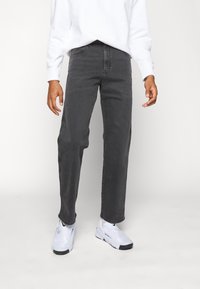 Jeans grises de denim, con un corte de pierna recta, detalles de costura y una cintura clásica. Combinados con zapatos blancos.