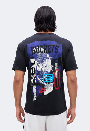 Muž s čiernymi vlasmi po ramená nosí čierne tričko s farebnou basketbalovou grafikou a slovom "BUCKETS" na chrbte.