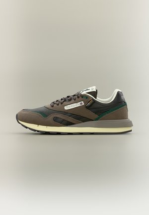 Zemi Reebok sporta apavi brūnā, melnā un zaļā krāsā ar baltu zolīti, priekšpusē ar auklām un zīmolu uz sāniem un papēža.