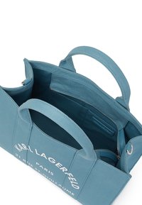 Borsa tote in tela blu con due manici e apertura superiore, dotata di una tasca con zip e testo bianco stampato sulla parte esterna.