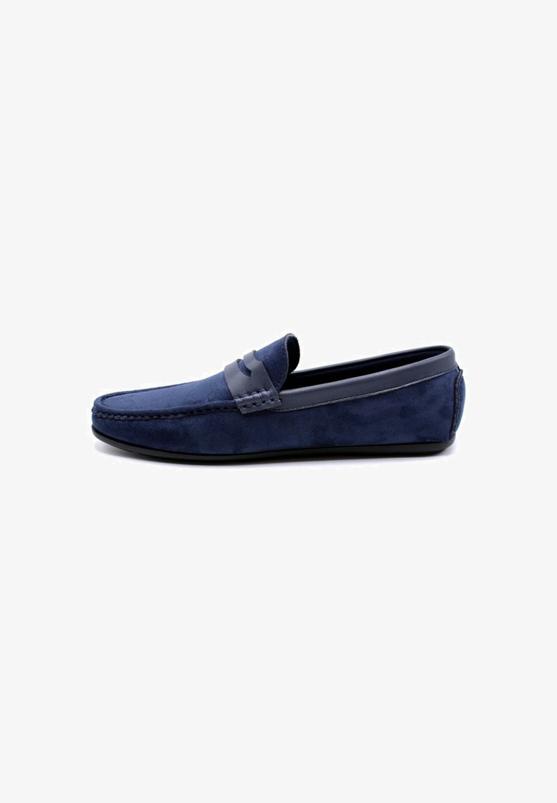 Mocassins en suède bleu marine avec une sangle en cuir lisse. Tige douce, bout rond et semelle plate en caoutchouc. Détails de couture simples le long du bord.