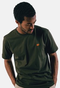 T-shirt en coton vert olive à manches courtes, col rond, avec un logo d'éléphant brodé orange sur la poitrine gauche.