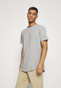 Gray cotton t-shirt with a crew neckline, short sleeves, relaxed fit, and a slightly curved hem. Worn with beige pants.