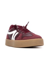 Zapatillas en color burdeos con textura de ante y cuero, detalles en blanco, puntera redonda y una suela de goma gruesa. Cordones del mismo color.