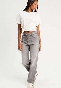 Grå højtaljede jeans med en afslappet pasform, der har et klassisk fem-lomme design. Kombineret med en hvid knyttet bomulds t-shirt.