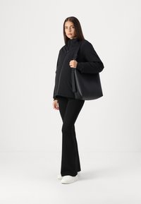 Black insulated jacket, black high-waisted flared pants, and white sneakers. The model holds a large black tote bag.