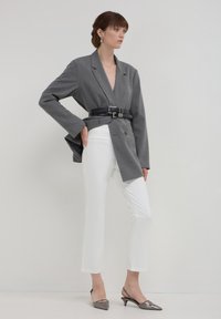 Blazer gris à rayures avec revers en V, taille ceinturée, associé à un pantalon droit blanc et des talons slingback gris brillants.