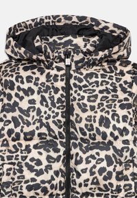 Lācēnu raksta pūkains jaka smilšu un melnā krāsā, ar rāvējslēdzēju un kapuci, ar gludu, vieglu tekstūru.