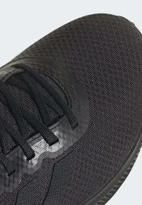 Czarne sportowe buty z chropowatą siateczką, płaskimi sznurowadłami i błyszczącymi akcentami. Projekt ma niskoprofilowy wygląd z okrągłym przodkiem.