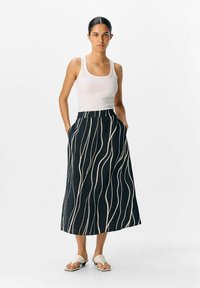 Jupe maxi marine avec des rayures ondulées blanches. Fabriquée en tissu léger, avec une taille haute et des poches latérales. Complétée par des sandales blanches.