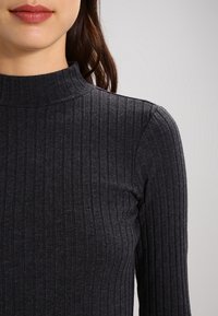 Grå ribbad polotröja med långa ärmar, som har en åtsittande passform och strukturerad tyg. Designen har en h ög krage och vertikala ränder.