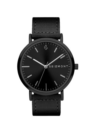 Svart analogt armbåndsur med minimalistisk design, hvite timemarkører, sølvfargede visere, "SEIZMONT"-logo på urskiven og svart teksturert stoffrem.