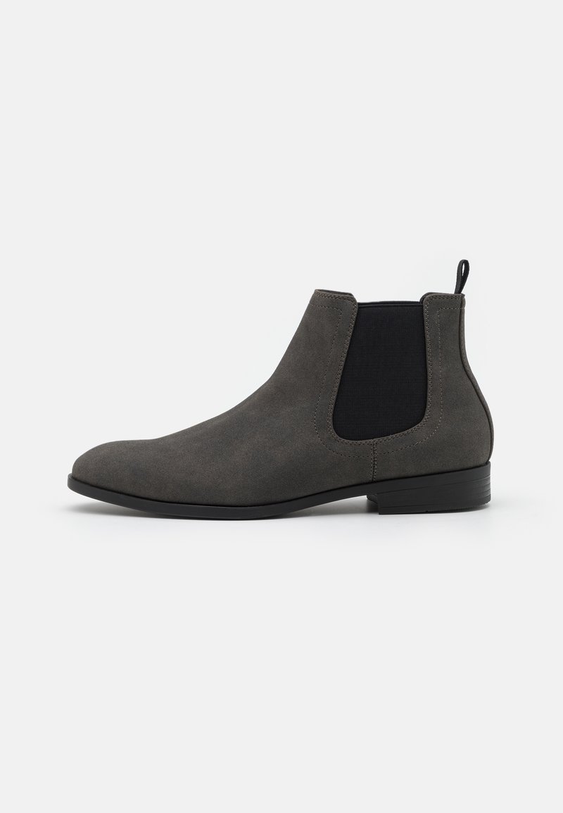 Bottine Chelsea en daim gris avec empiècement élastique noir sur le côté et petit talon noir sur fond blanc.