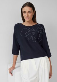 Top en tricot bleu marine à manches trois-quarts, présentant un design de points floraux abstraits en argent au niveau du col. Texture lisse.