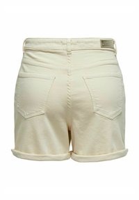 Shorts en denim couleur crème avec ourlets retroussés, comportant deux poches arrière et une petite étiquette de marque près de la taille. Design simple et minimaliste.