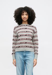 Γκρι πλεχτό πουλόβερ με έντονο επαναλαμβανόμενο σχέδιο κειμένου "JOOP! JEANS" σε μαύρο και κόκκινο. Πλεκτές μανσέτες και τελείωμα με ριμπ ύφανση, άνετη εφαρμογή. Ανοιχτόχρωμο τζιν παντελόνι.