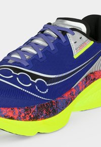 Μπλε αθλητικό παπούτσι με μοβ κορδόνια, μαύρο και λευκό λογότυπο, κόκκινο-μαύρη σπογγώδη ενδιάμεση σόλα και σόλα νέον κίτρινου χρώματος.