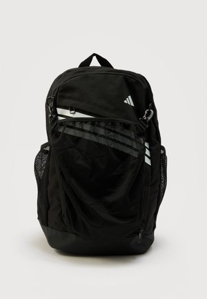 Mochila negra con bolsillo frontal de malla, bolsillos laterales de malla y franjas diagonales blancas, de pie sobre un fondo liso.