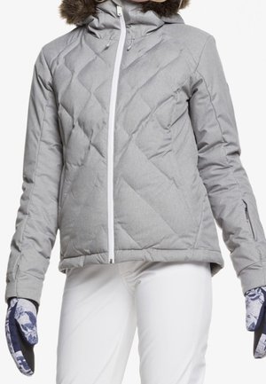 Kviltet grå jakke med hætte, der har en aftagelig faux fur trim og hvid lynlås. Sammen med mønstrede handsker og hvide bukser.