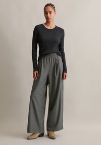 Dunkelgrauer gerippter Pullover mit langen Ärmeln, kombiniert mit locker sitzenden grünen Karohosen und beigen Stiefeletten. Weiche Textur und lässiges Design.