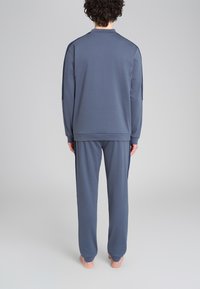 Tuta atletica grigia composta da un top a maniche lunghe e pantaloni coordinati, realizzata in un tessuto liscio, con una vestibilità comoda e dettagli di cucitura discreti.