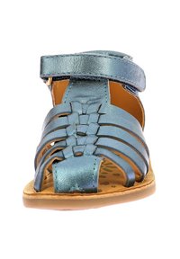 Sandal de cuero metálico azul con correas trenzadas, diseño de punta abierta y correa en el tobillo. Suela de color marrón claro con plantilla texturizada.