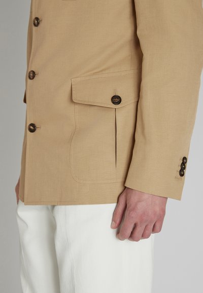 Giacca in misto lino color marrone chiaro, con taschino sul petto, tre bottoni e colletto a punta. Rifinita con una silhouette pulita e spacchi laterali.