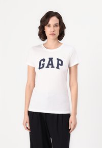 Hvit bomull t-skjorte med et marineblått "GAP" logo på forsiden. Korte ermer og en klassisk rund hals.