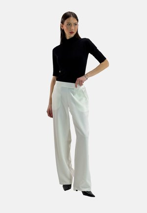 Top corto nero a maniche corte abbinato a pantaloni bianchi a gamba larga con tasche laterali, texture liscia e vestibilità sartoriale. Scarpe nere appuntite.