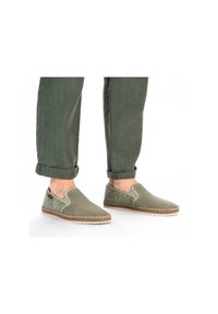 Scarpe slip-on verde chiaro con superiore in rete e dettagli testurizzati. Bordo in juta circostante, abbinate a pantaloni verdi arrotolati.