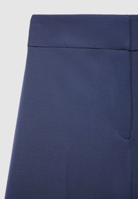 Pantalon bleu marine ajusté avec une texture lisse, doté d'une ceinture avant plate et d'un détail de poche latérale.