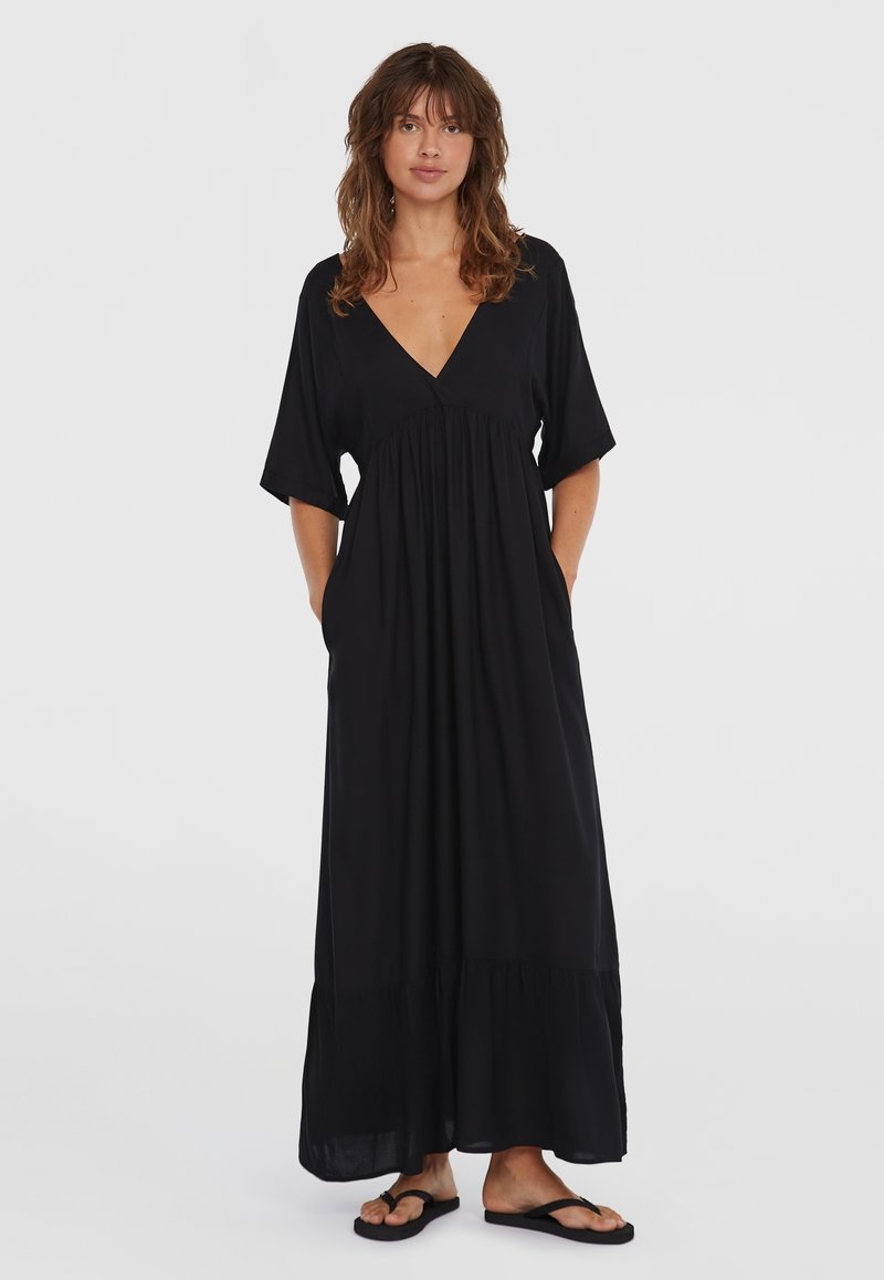 Svart maxi-kjole med korte batwing-ermer, V-halsdesignet, samlet midje, sidelommer og en flowy lagdelt skjort. Stylet med flip-flops.