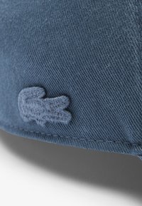 Gorra de algodón azul con un logo de cocodrilo bordado, tejido texturizado y costuras visibles a lo largo del borde.