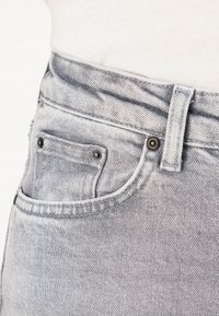 Pogled od blizu na žep svetlo prane jeanske hlače z zakovicami in zanko za pas, oblečeno z zataknjenim belim srajcem.