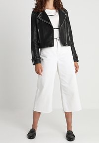 Svart läderbikerjacka med silverdetaljer, vita cropped vida byxor och svarta loafers med nitar.