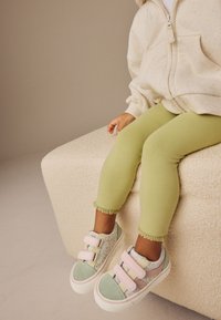 Világoszöld leggings csipkés díszítéssel, pasztellszínű, virágmintás sportcipőkkel, tépőzáras pántokkal párosítva. Textúrált, puha anyag.