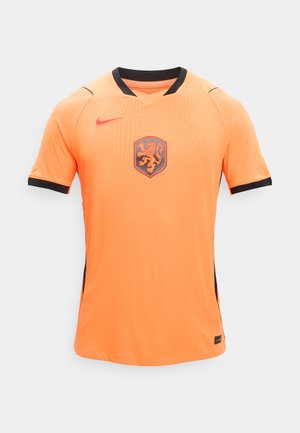 Oranssi lyhythihainen jalkapallopaita, jossa musta kaulus ja hihansuut, leijonakuvio rintakehässä sekä punainen Nike Swoosh -logo rinnassa.