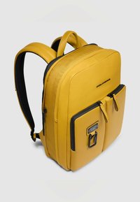 Gele leren rugzak met gevoerde achterkant, twee voorvakken, ritssluiting en zwarte accenten. Soepele textuur, moderne rechthoekige vorm.