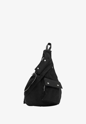 Mustat kangaskassi, jossa on useita vetoketjullisia osastoja, napinappikiinnityksellisiä taskuja ja yksi olkahihna. Omistaa sileän pinnan.