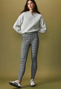 Grå sweatshirt med sænkede skuldre, parret med høj talje sorte og hvide ternede leggings og hvide sneakers med sorte striber.