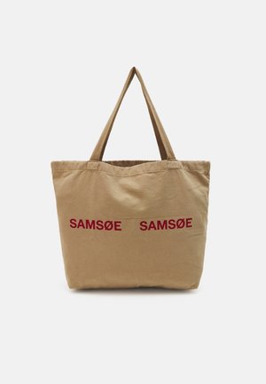 Beige stoffen draagtas met twee handvatten en rode tekst "SAMSØE SAMSØE" op de voorkant gedrukt, gefotografeerd tegen een witte achtergrond.